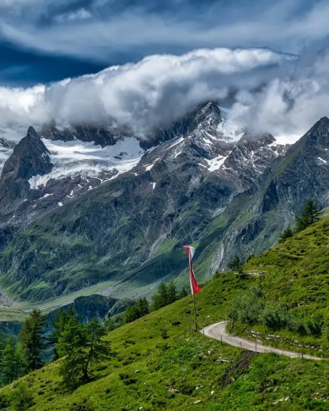 Alpine valley with snow-capped peaks, green slopes and a mountain path